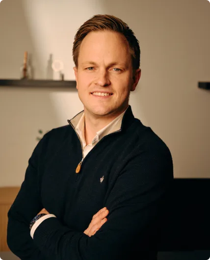 Man with dark hair and crossed arms wearing navy quarter-zip sweater over white shirt