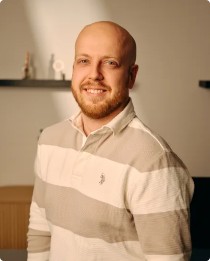 Bald man with beard smiling wearing beige and white striped polo shirt