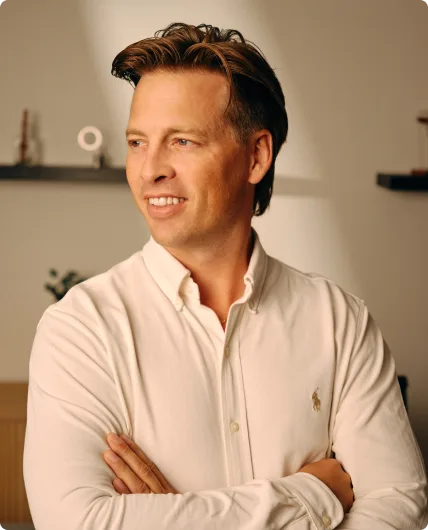 Man with dark hair smiling and crossed arms wearing light beige button-up shirt
