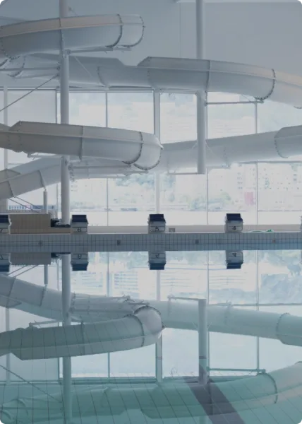 Indoor water park with multiple twisting water slides and a swimming pool with lane dividers, viewed through large windows.
