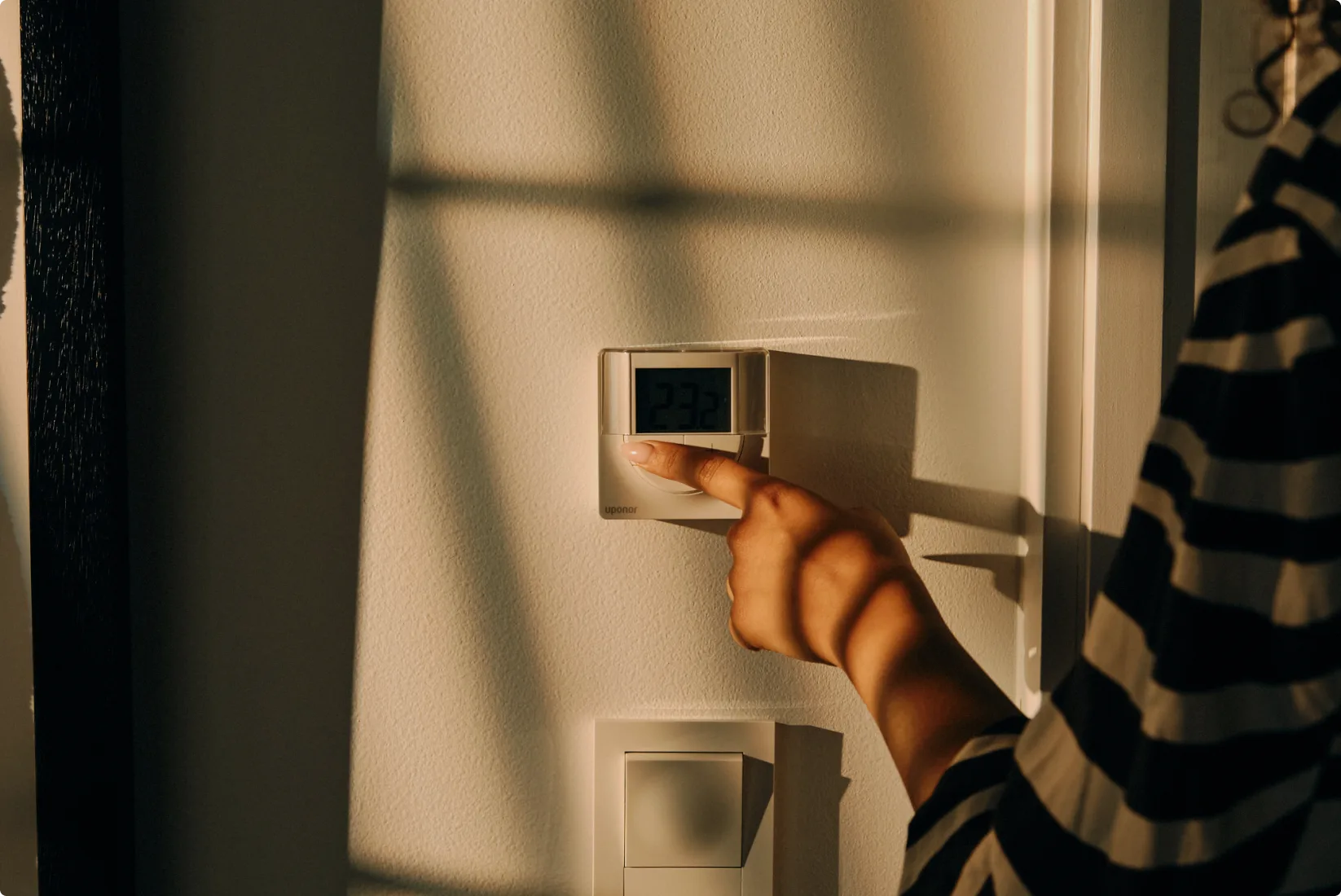 Hand adjusting a digital thermostat on a white wall